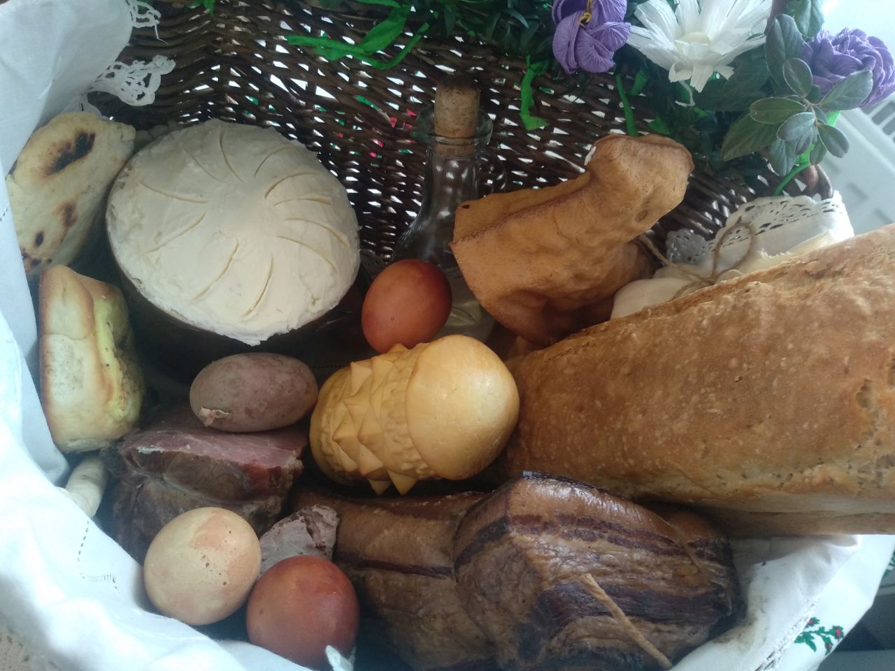 żywność w koszyku, chleb z formy, sery, jajka barwione na ciemnoczerwono, wędliny, butelka z wodą i inne wiktuały