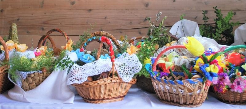 Kilka konkursowych koszyczków wielkanocnych w rzędzie. Przystrojone w białe serwety, kwiaty i ozdoby z bibuły i zielone gałązki