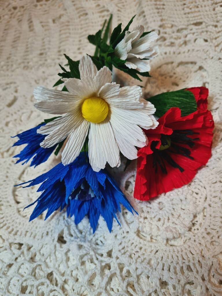 trzy kwiaty z bibuły na białym obrusie