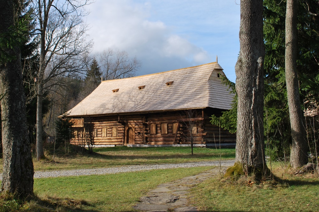 Dwór Moniaków - drewniany budynek z nowym dachem widoczny spomiędzy drzew